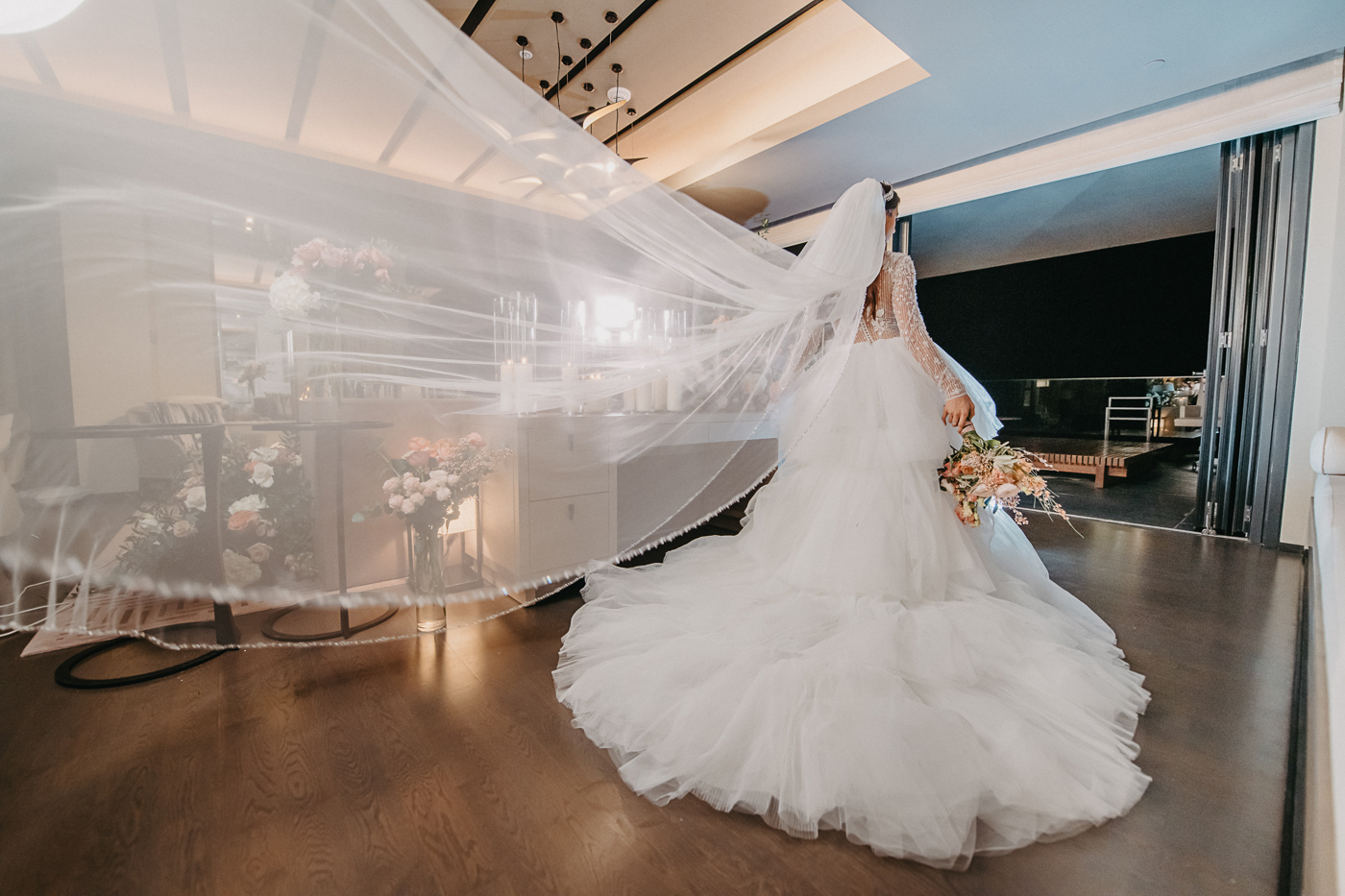 Bride gazes outdoors, veil flowing, elegant room, flowers; Banyan Tree Dubai wedding ambiance.